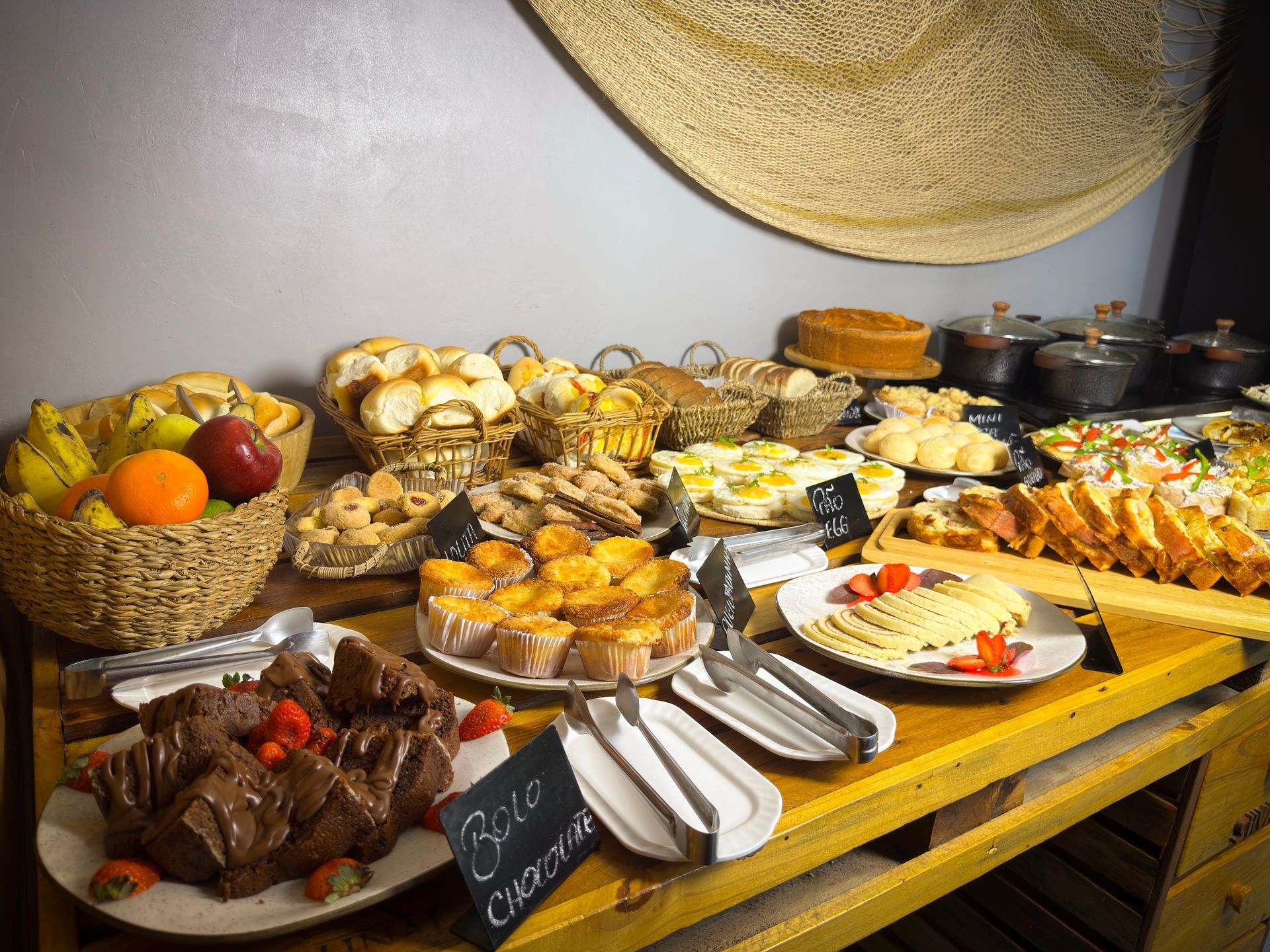 Mesa de bufê com uma variedade de doces, frutas e sobremesas dispostas em bandejas e travessas.