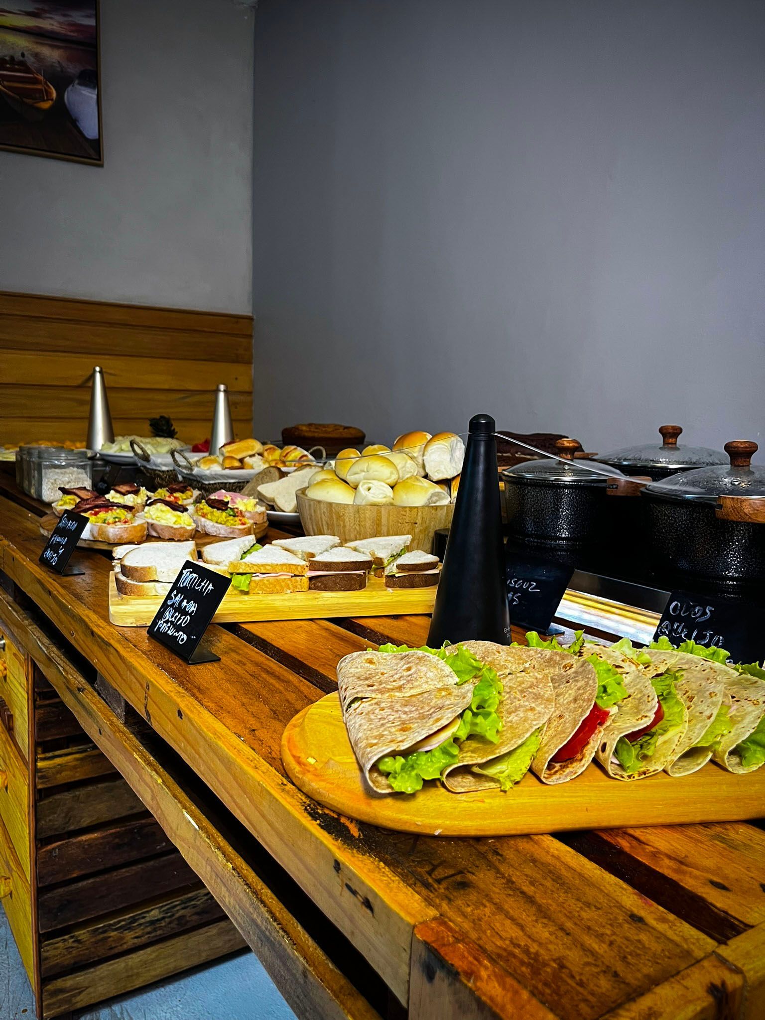 Mesa de buffet com sanduíches, pães e pratos variados em um ambiente de restaurante.