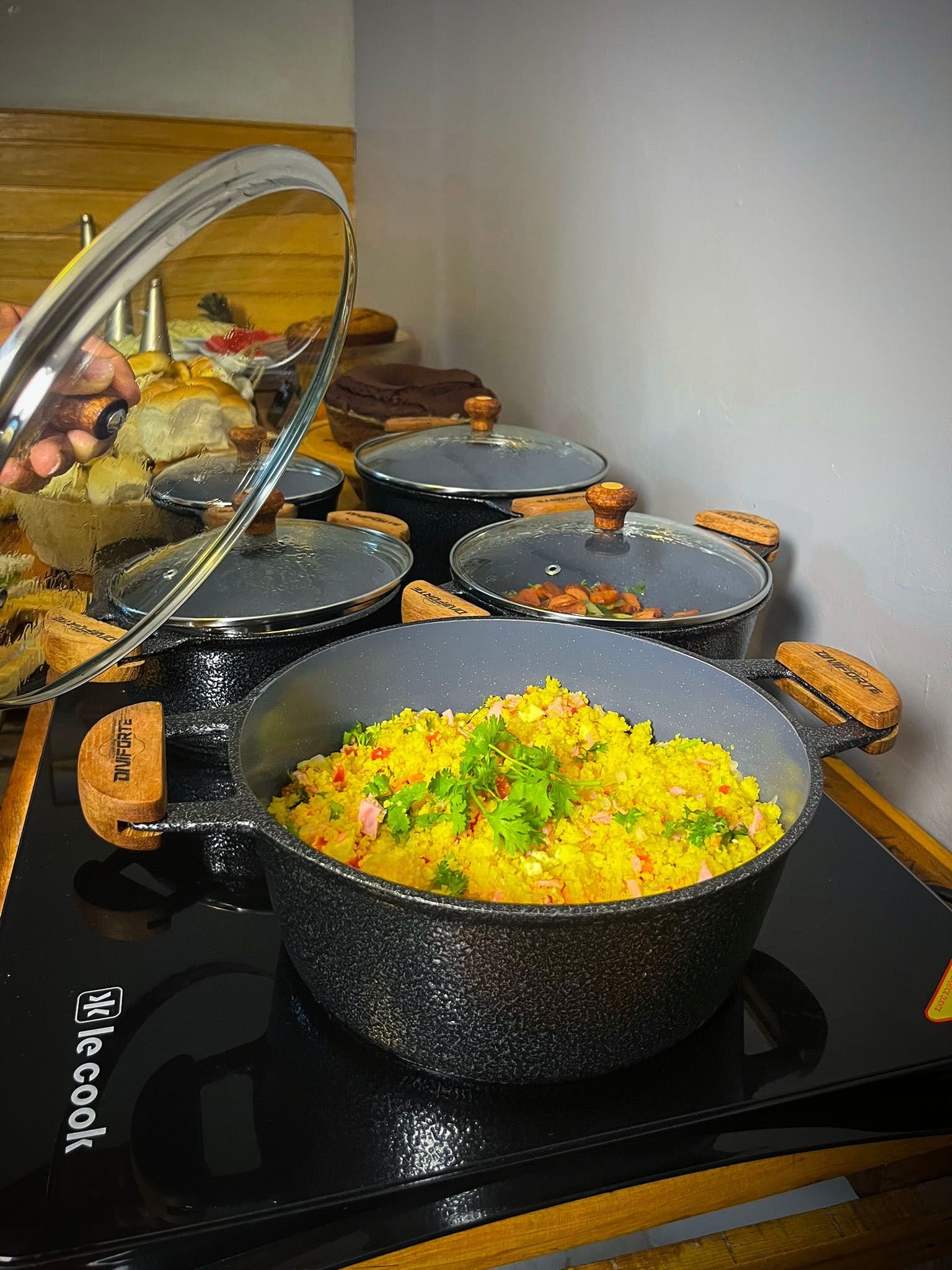 Três panelas de arroz amarelo com ensopado fervem em fogo brando no fogão, com uma das panelas em primeiro plano.