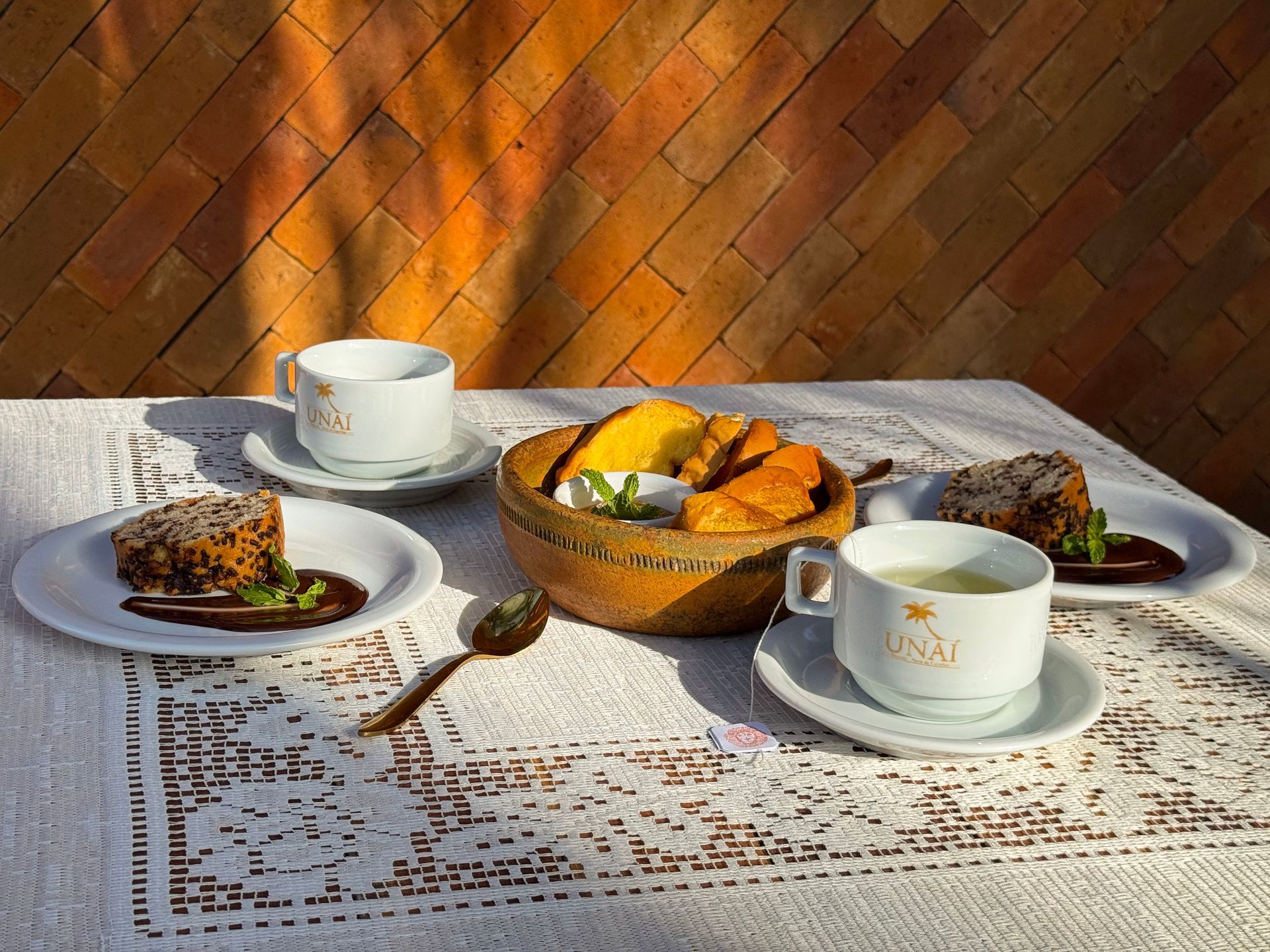 Café da manhã posta sobre a mesa com xícaras, frutas e torradas sob a luz quente do sol.