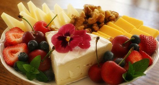 A plate of cheese , fruit and nuts on a table.