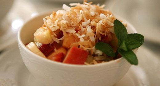 A bowl of fruit salad with coconut and mint on a plate.