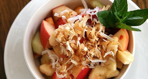 A bowl of fruit salad with coconut and mint on a white plate.