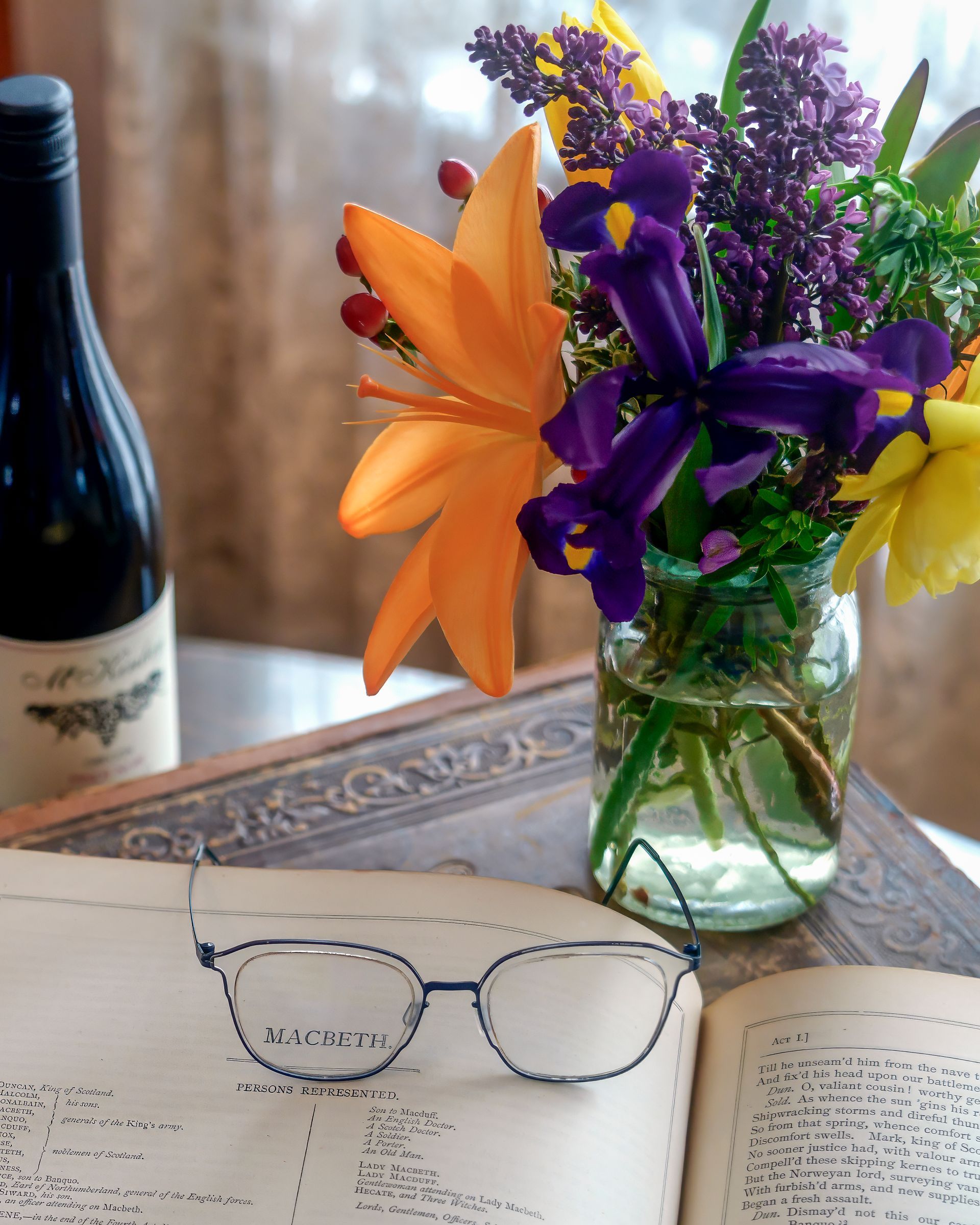 A pair of glasses sits on a book next to a vase of flowers