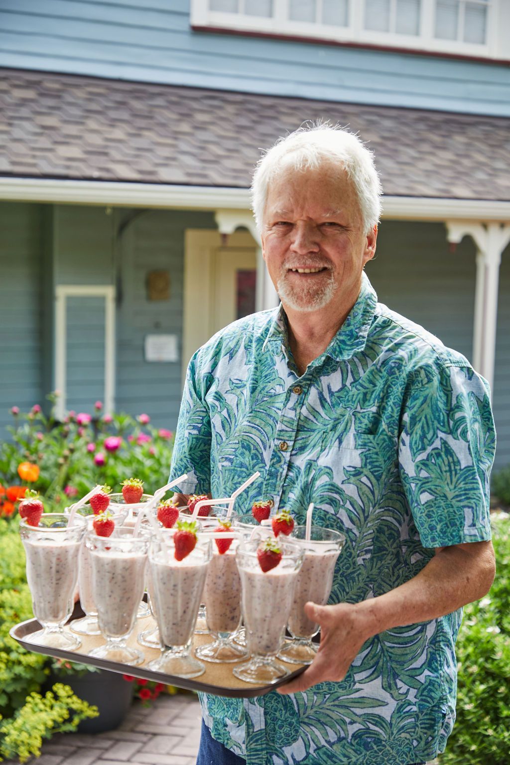 A man is holding a tray of milkshakes with strawberries on top.