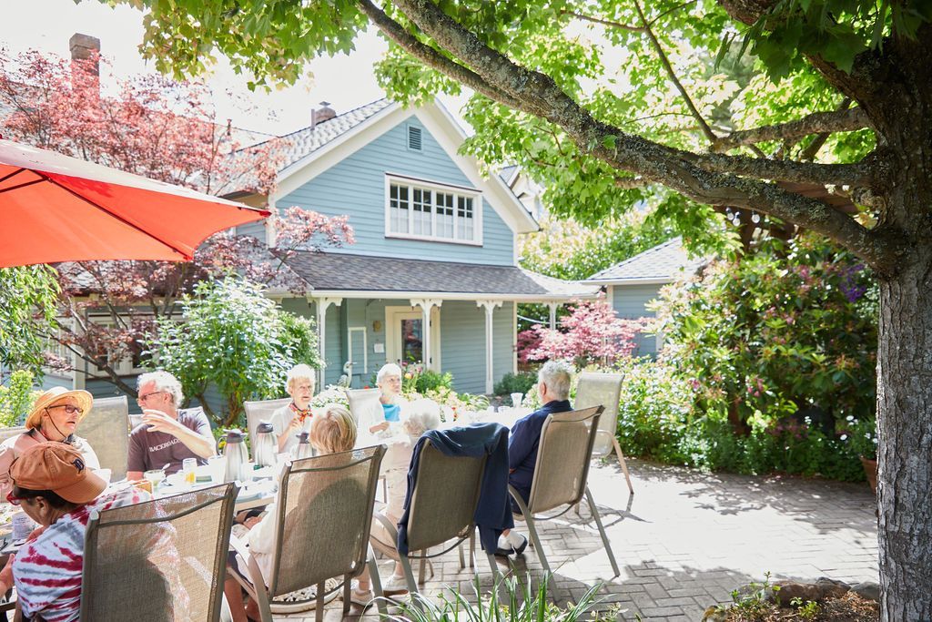 A group of people are sitting at a table under an umbrella in front of a house.