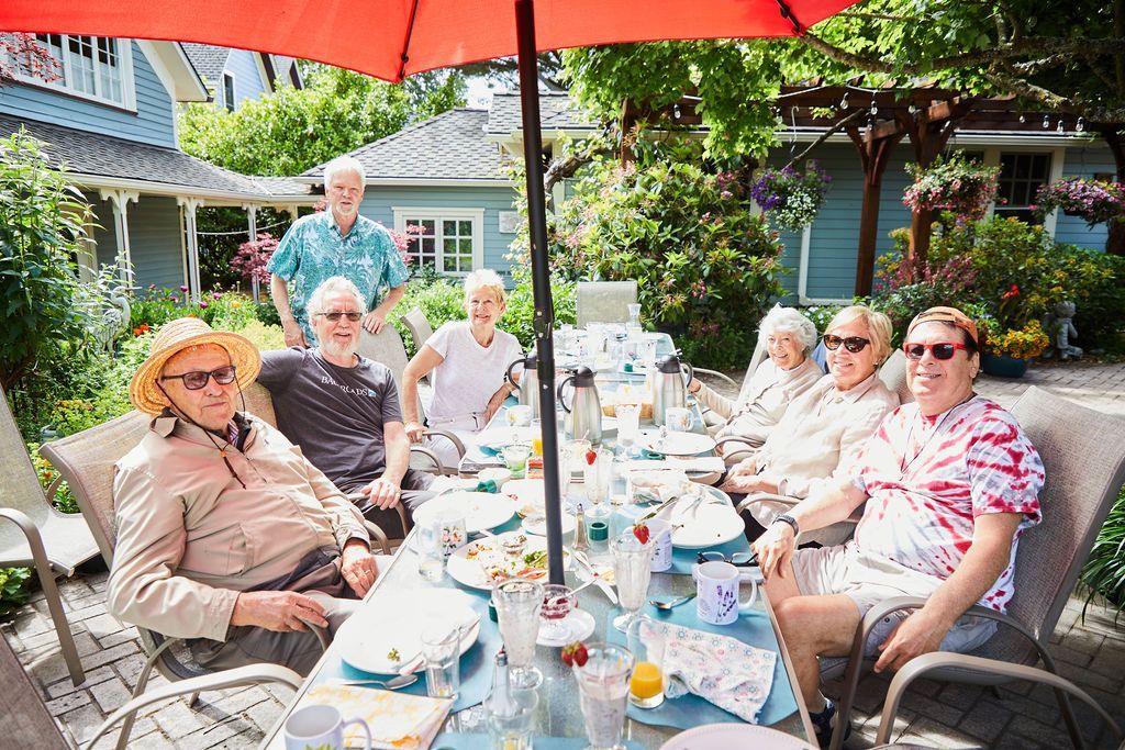 A group of people are sitting at a long table under an umbrella.