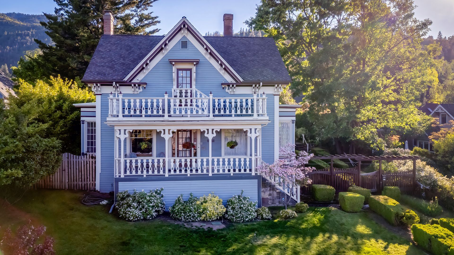 An aerial view of a large blue house with a large porch surrounded by trees.
