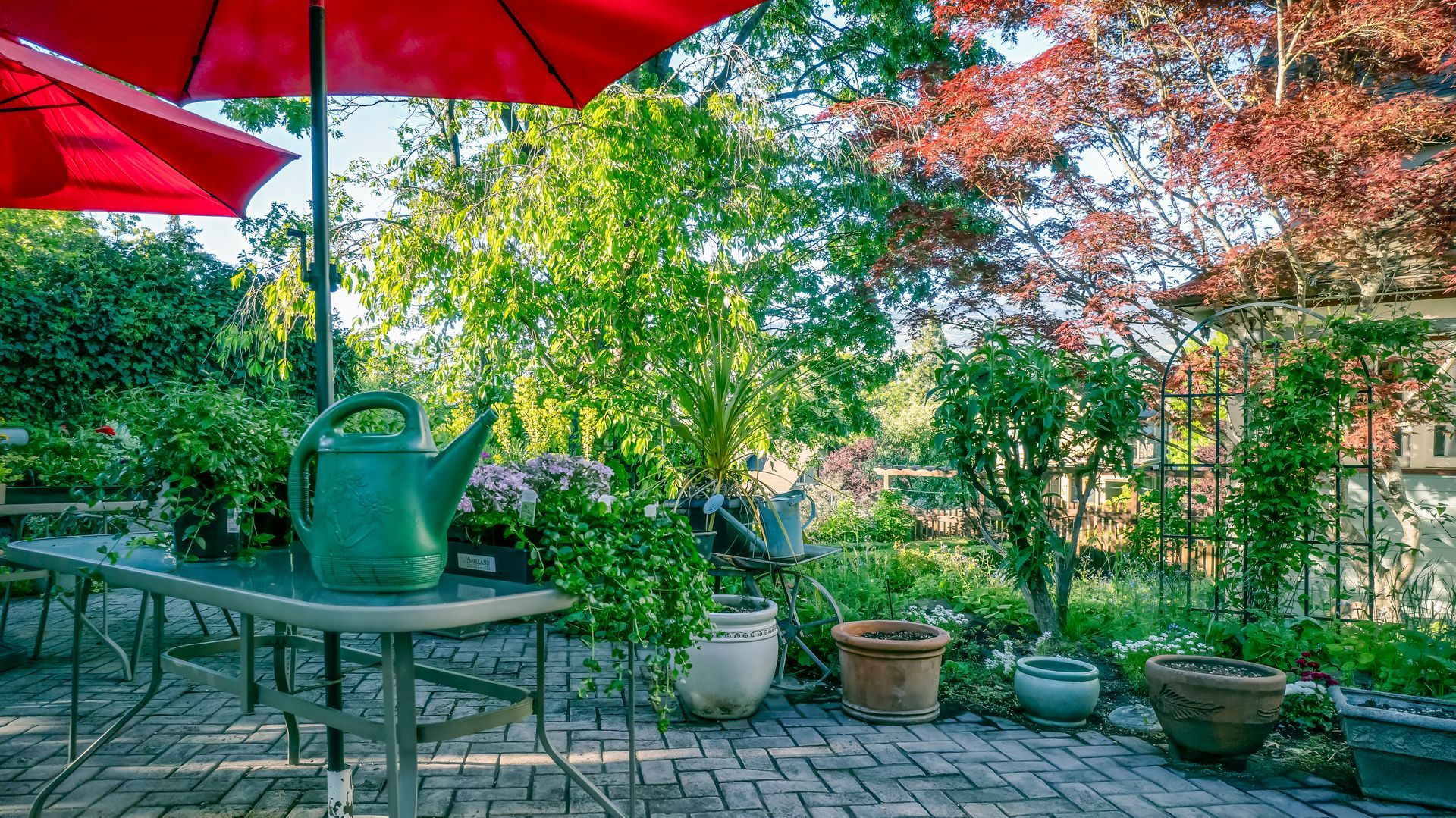 A watering can is sitting on a table under an umbrella on a patio.