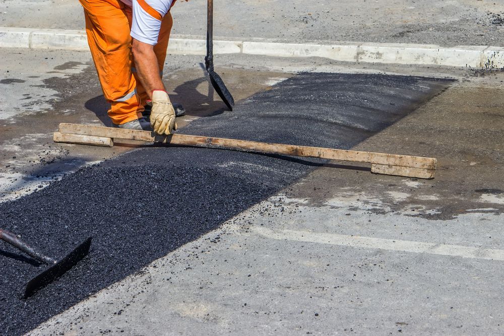 Worker in Orange Pants Paving a Road With Asphalt, Using a Long Wooden Leveler — Slash Mulch Co in Googa Creek, QLD