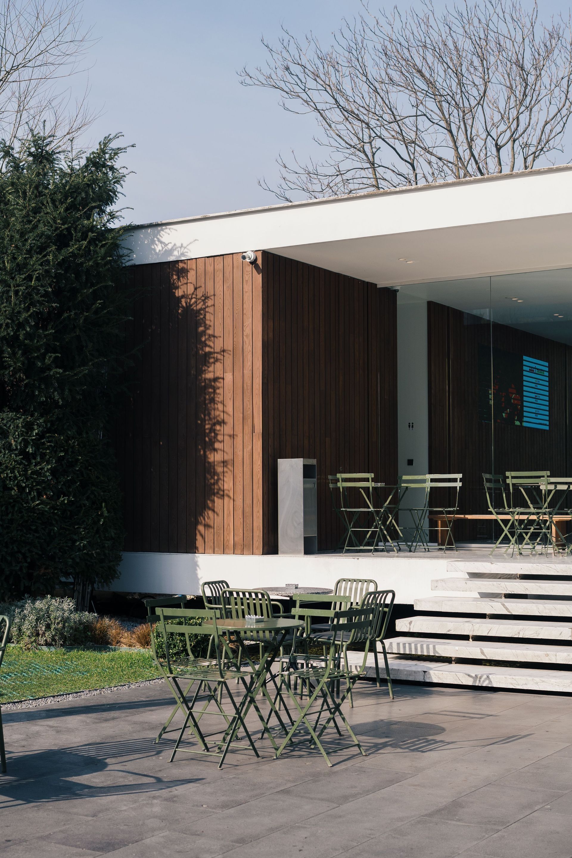 Outdoor patio with metal tables and chairs beside a modern building entrance