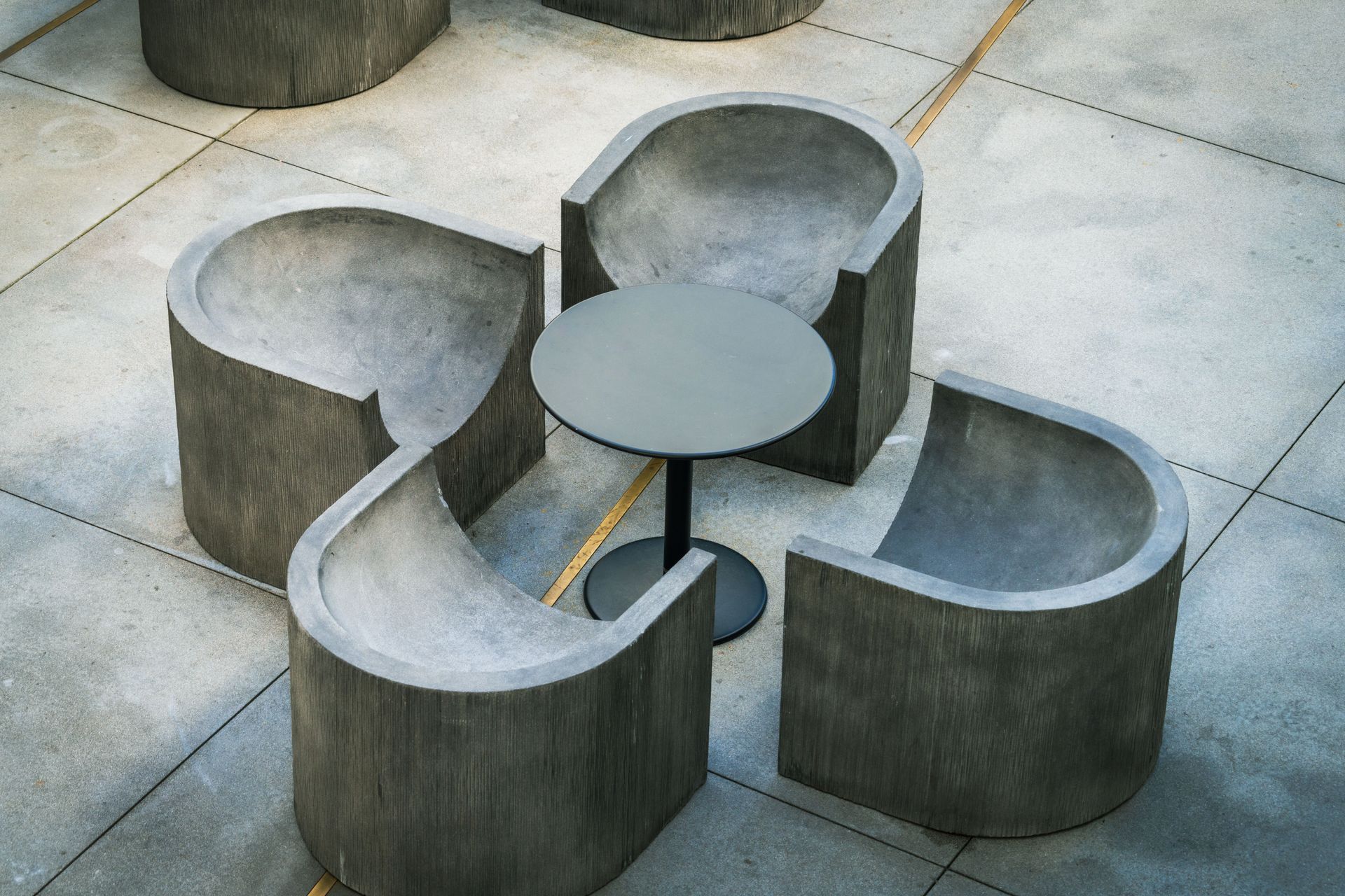 Outdoor concrete bench set with curved seats around a small round table on tiled pavement