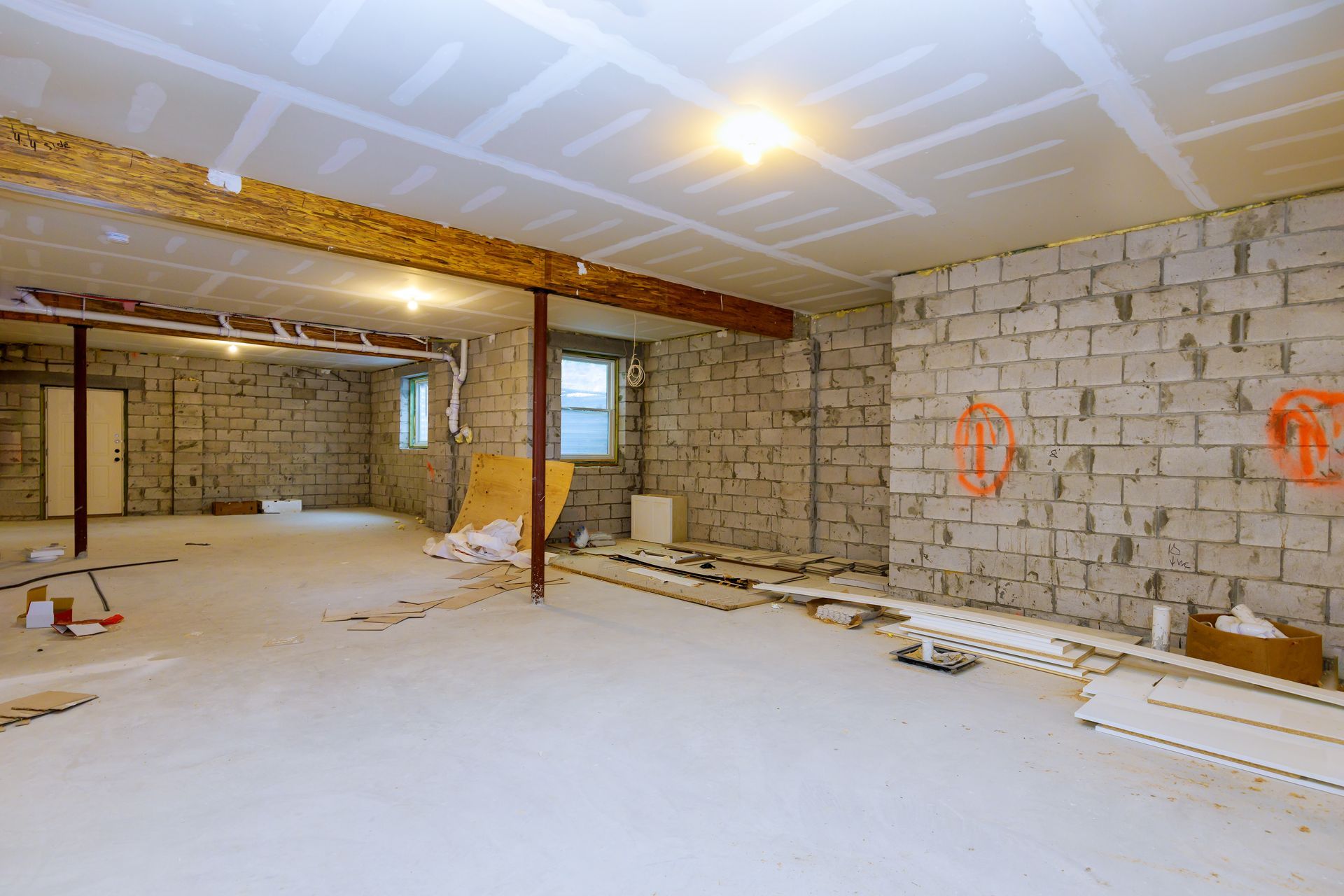 Unfinished basement interior with exposed block walls, beams, and construction materials on the floor.