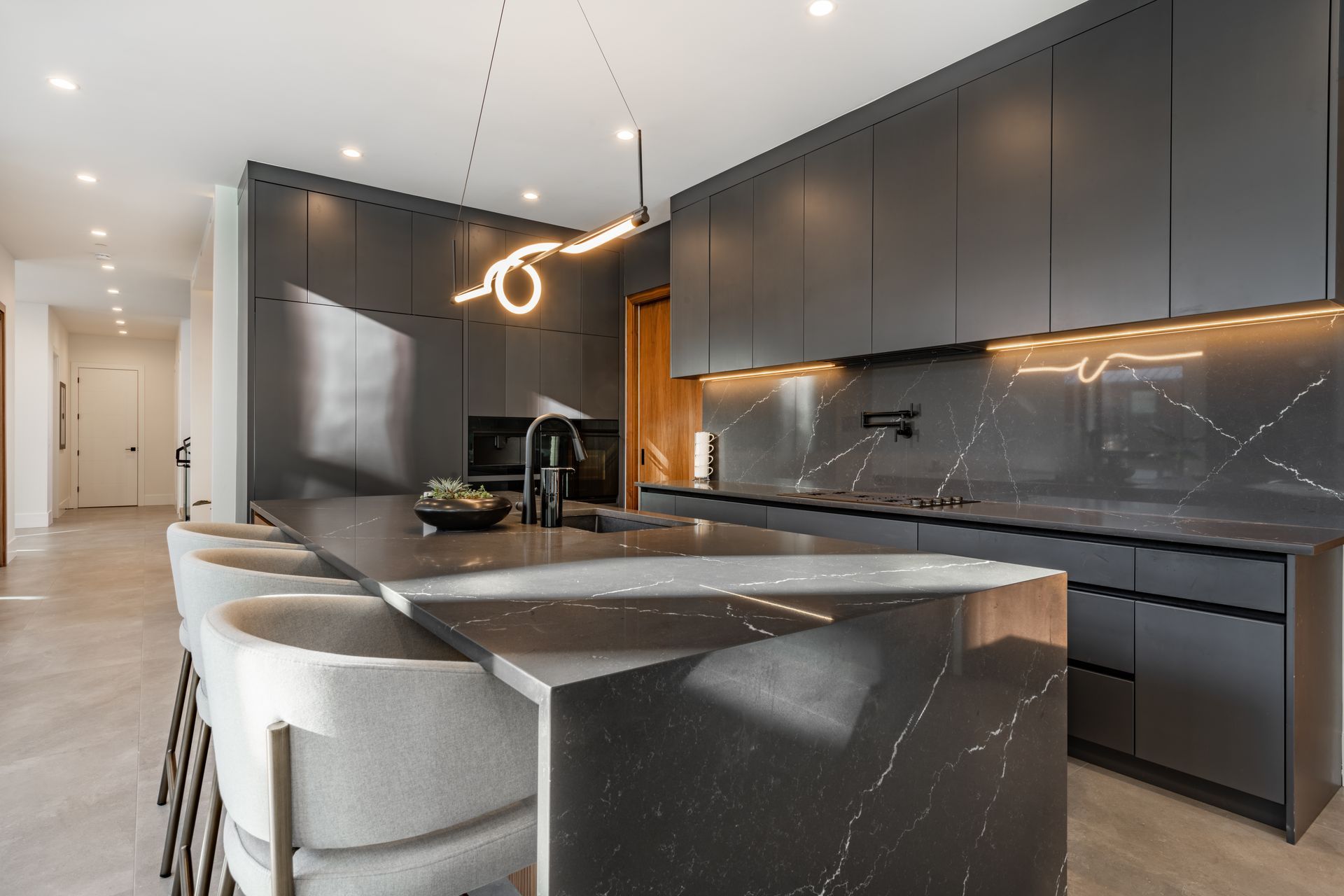 Modern kitchen with dark cabinetry, marble island, pendant lights, and built-in sink and cooktop.