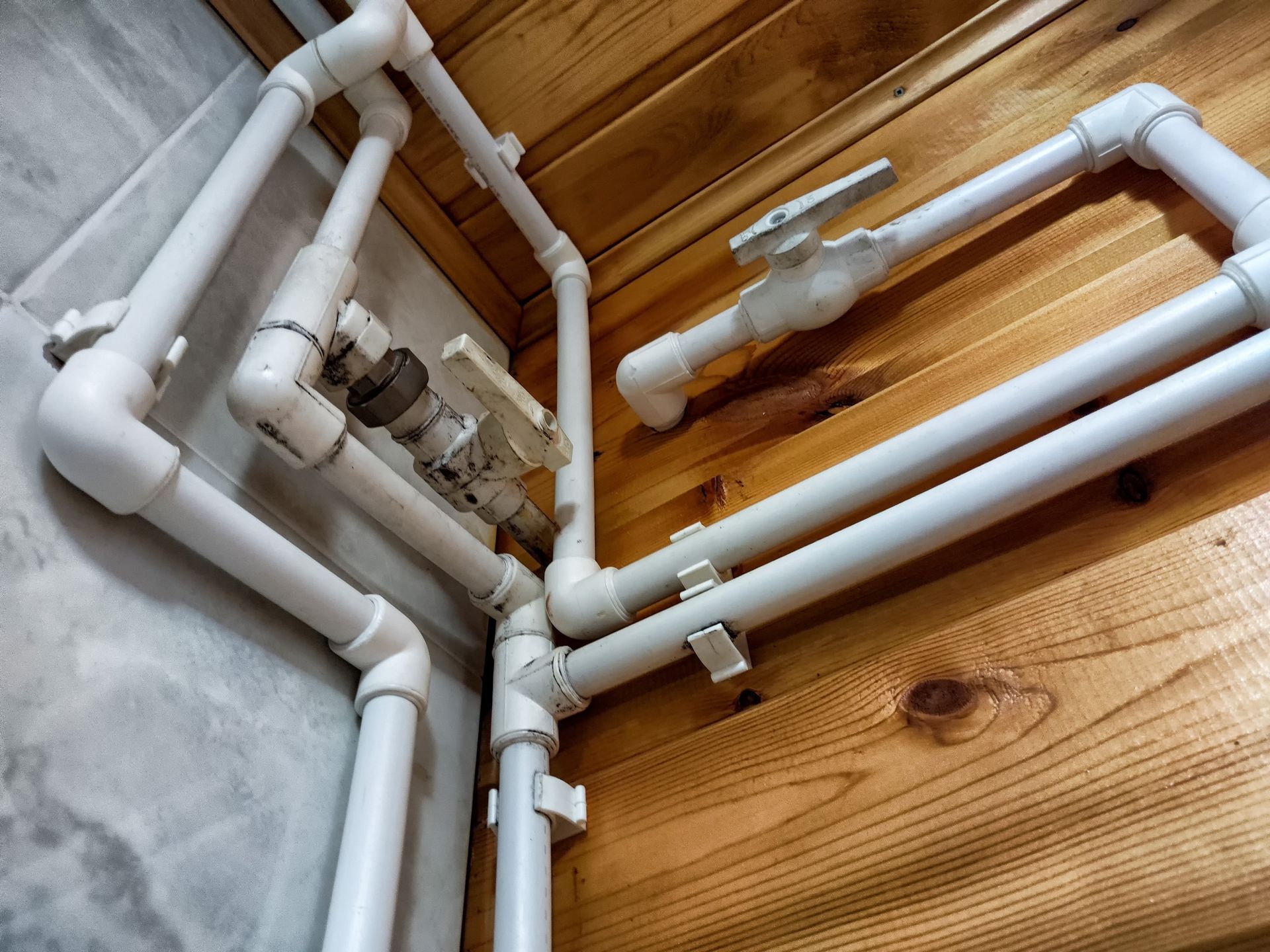 White PVC pipes and valves mounted against a wood-paneled wall, viewed from below.