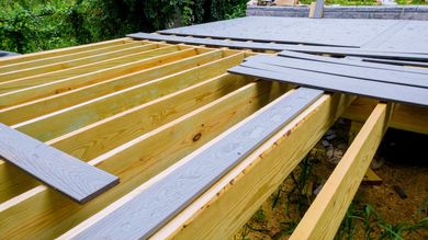 Wooden deck frame under construction with gray boards laid across the joists outdoors.