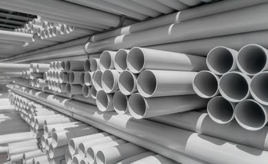 Stacks of gray PVC pipes stored on warehouse shelves in perspective view