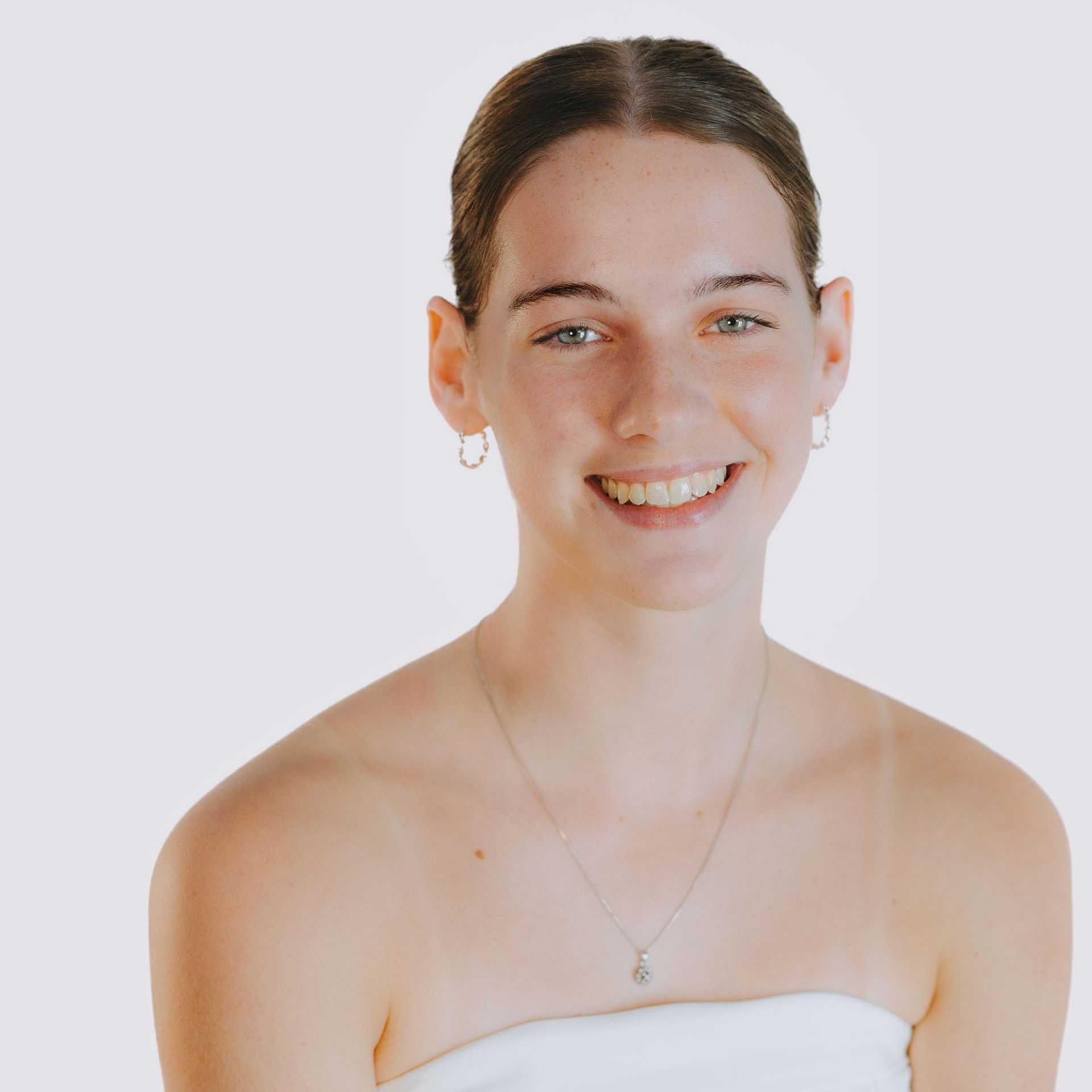 A young woman is smiling and wearing a necklace and earrings.