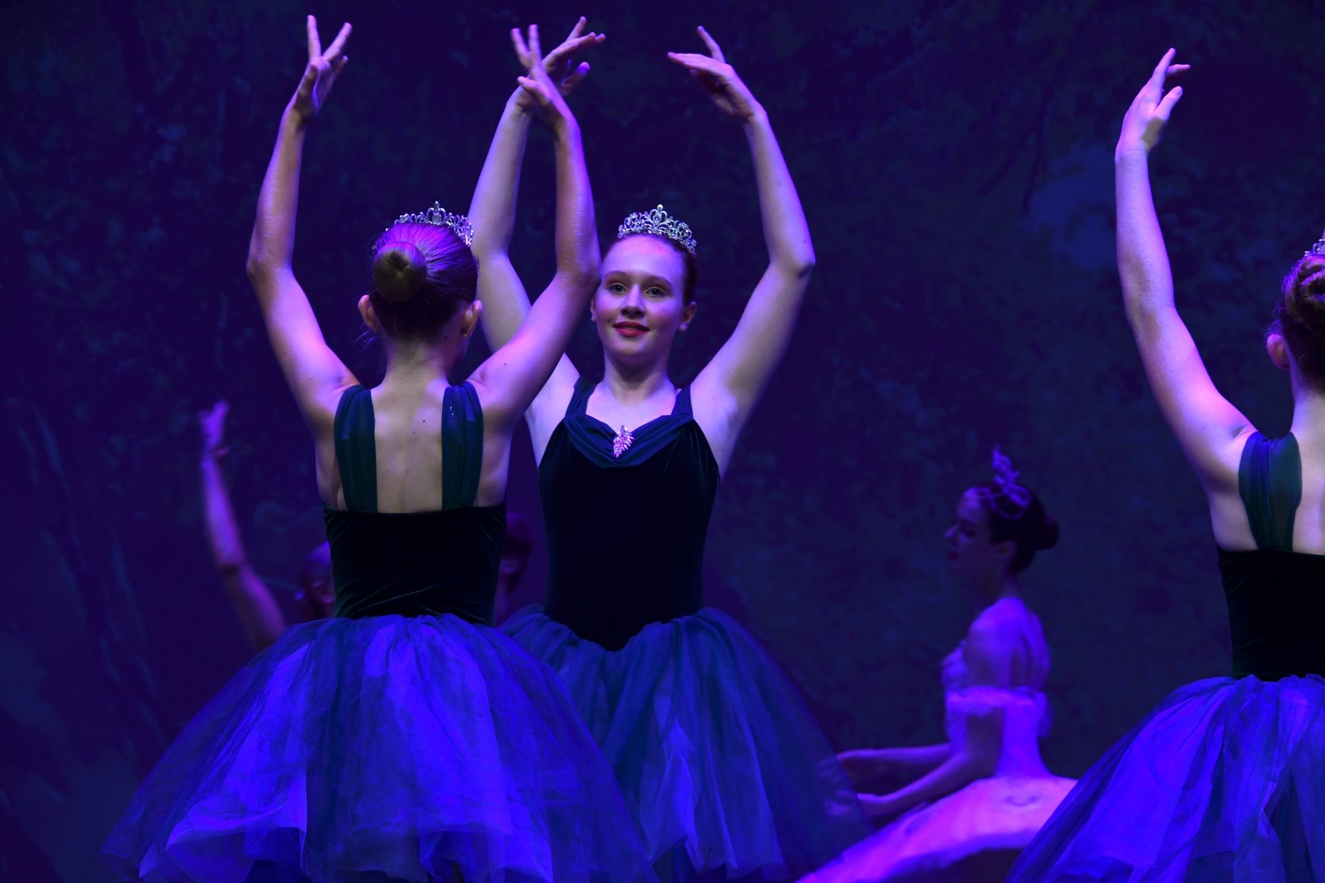 A group of ballerinas are dancing on a stage with their arms in the air.