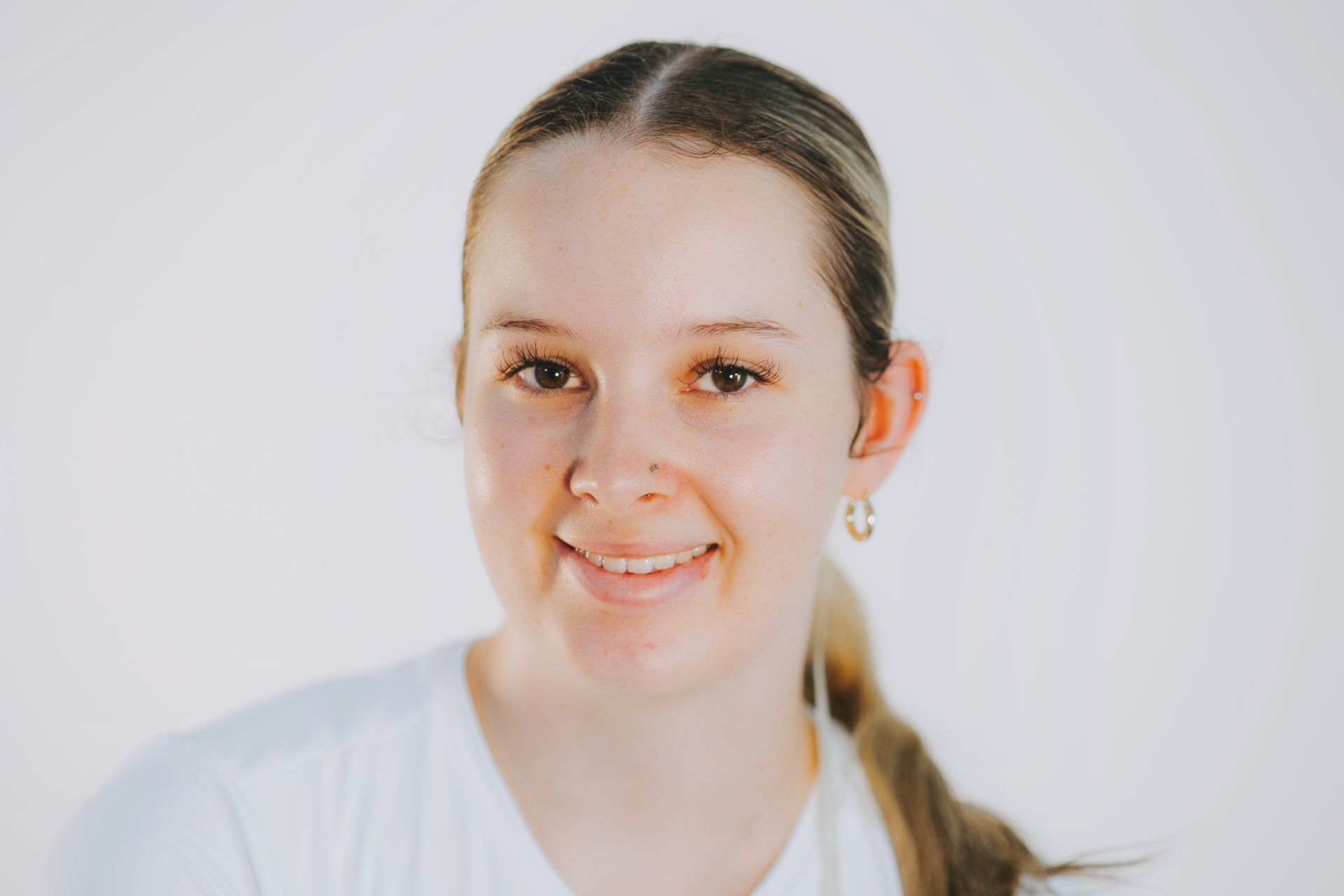 A young woman wearing a white shirt and earrings is smiling for the camera.