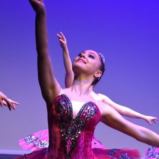 A woman in a pink tutu is dancing on a stage.