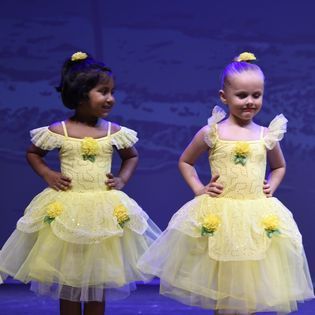 Two little girls in yellow dresses are standing next to each other on a stage.