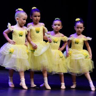 A group of young girls in yellow dresses are standing on a stage.