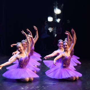 A group of young girls in purple tutus are dancing on a stage.