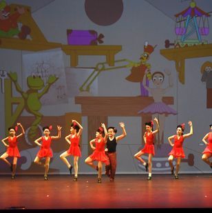 A group of young girls in red dresses are dancing on a stage.
