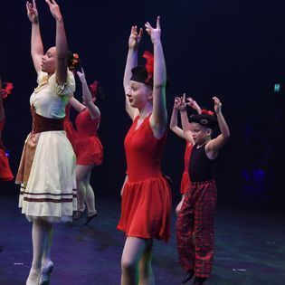 A group of young girls are dancing on a stage with their arms in the air.