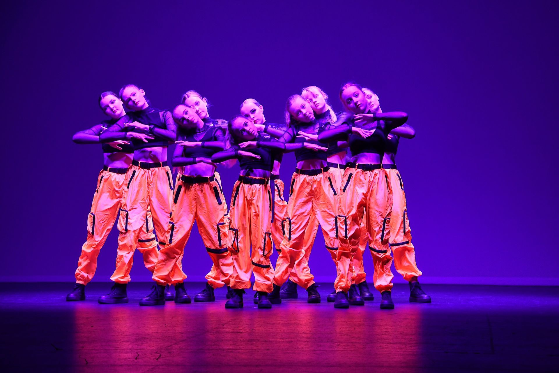 A group of dancers are performing on a stage in front of a purple background.