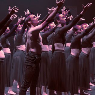 A group of dancers are standing on a stage with their arms in the air.