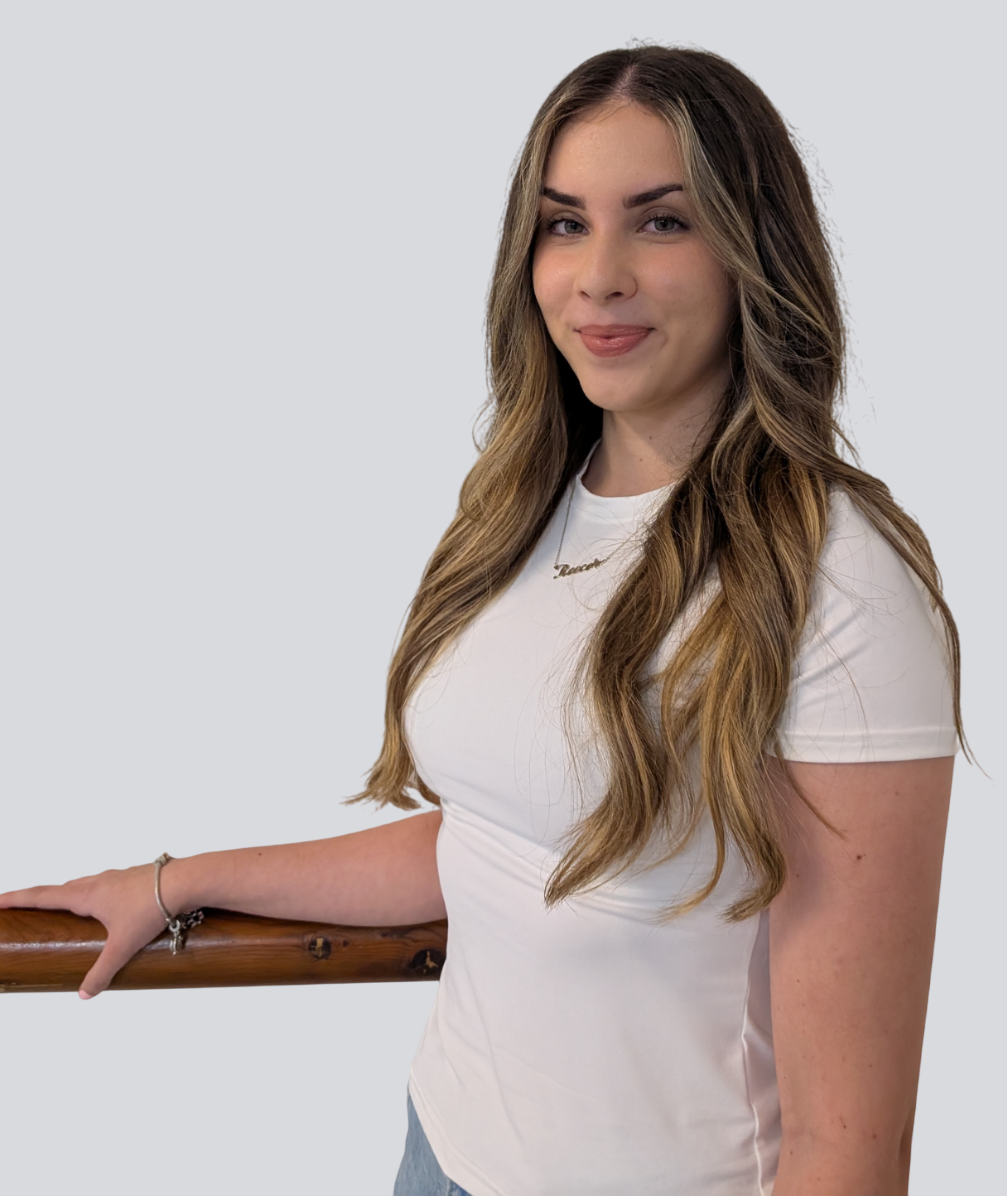 A woman in a white shirt is standing next to a wooden railing.