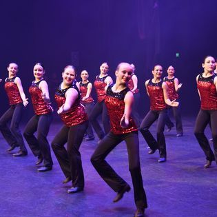 A group of women in red sequined tops and black pants are dancing on a stage.
