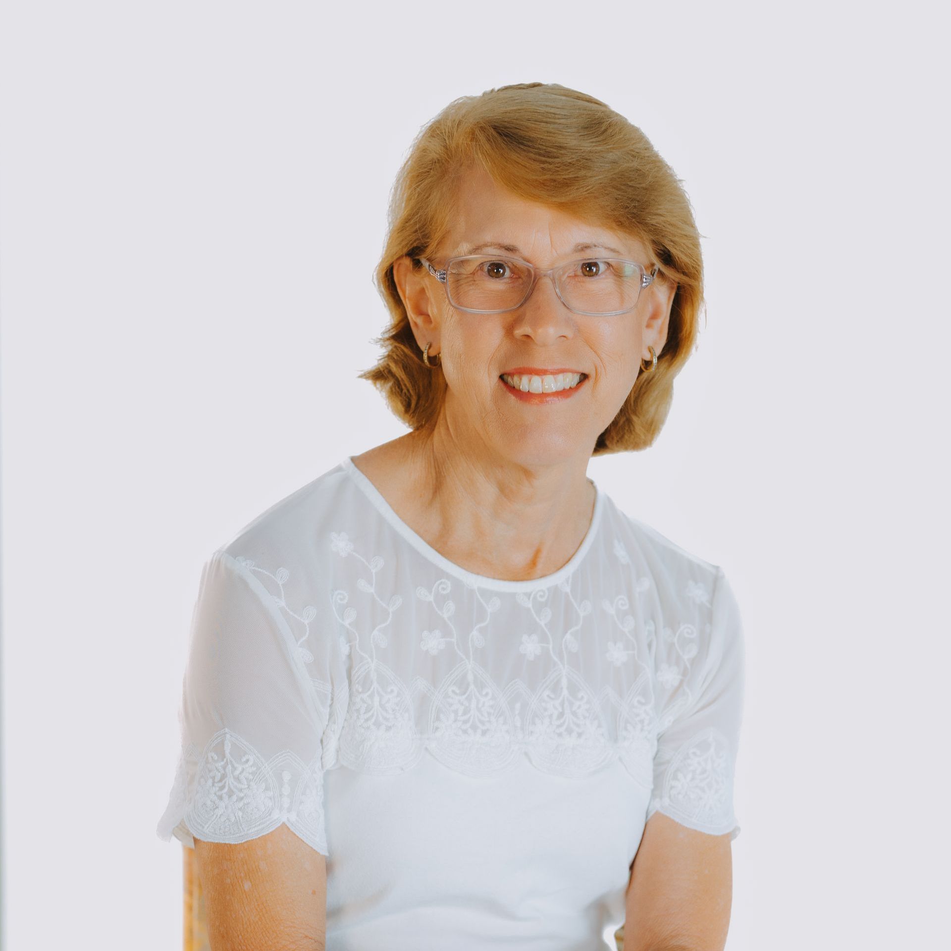 A woman wearing glasses and a white shirt is smiling for the camera.