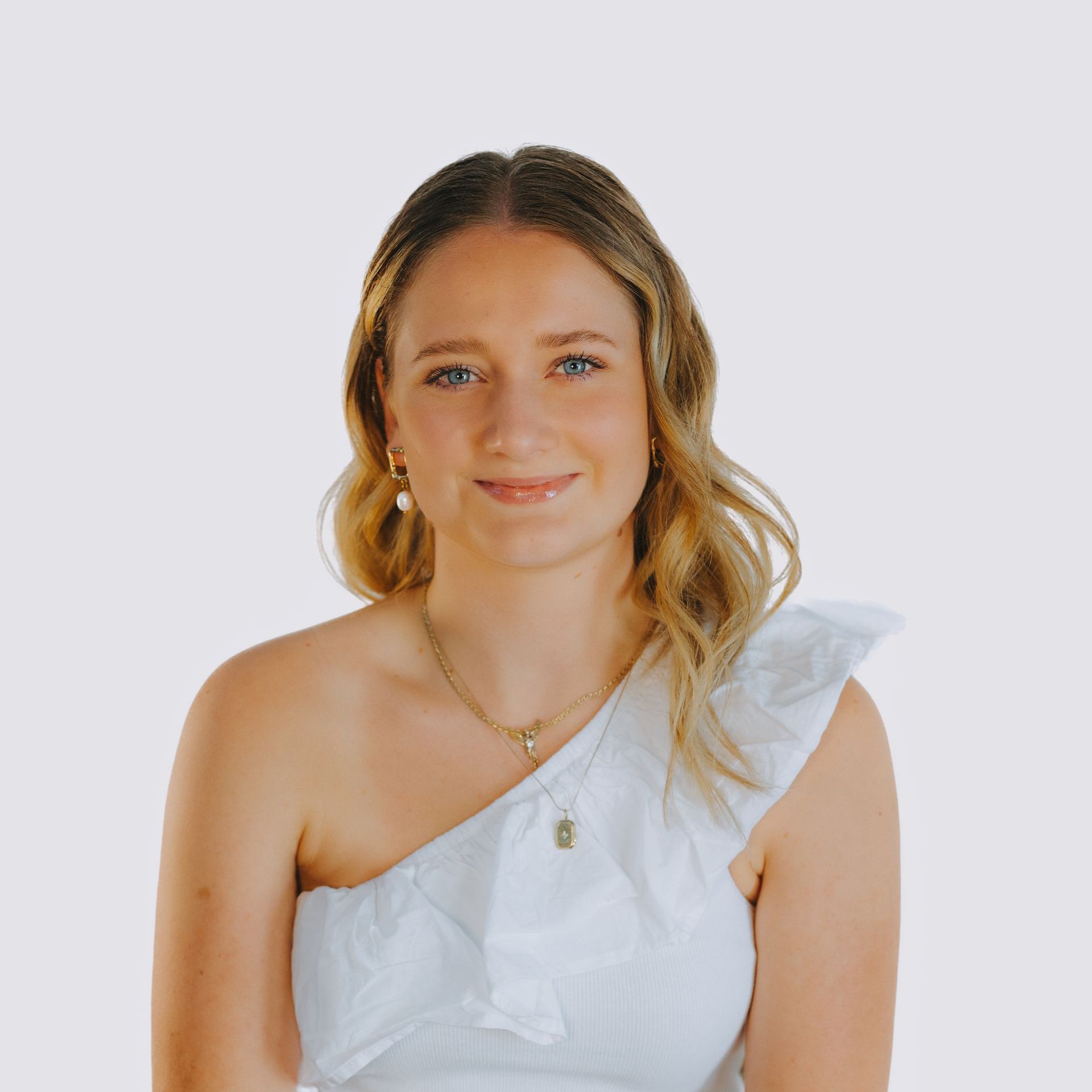 The woman is wearing a white one shoulder dress and a necklace.