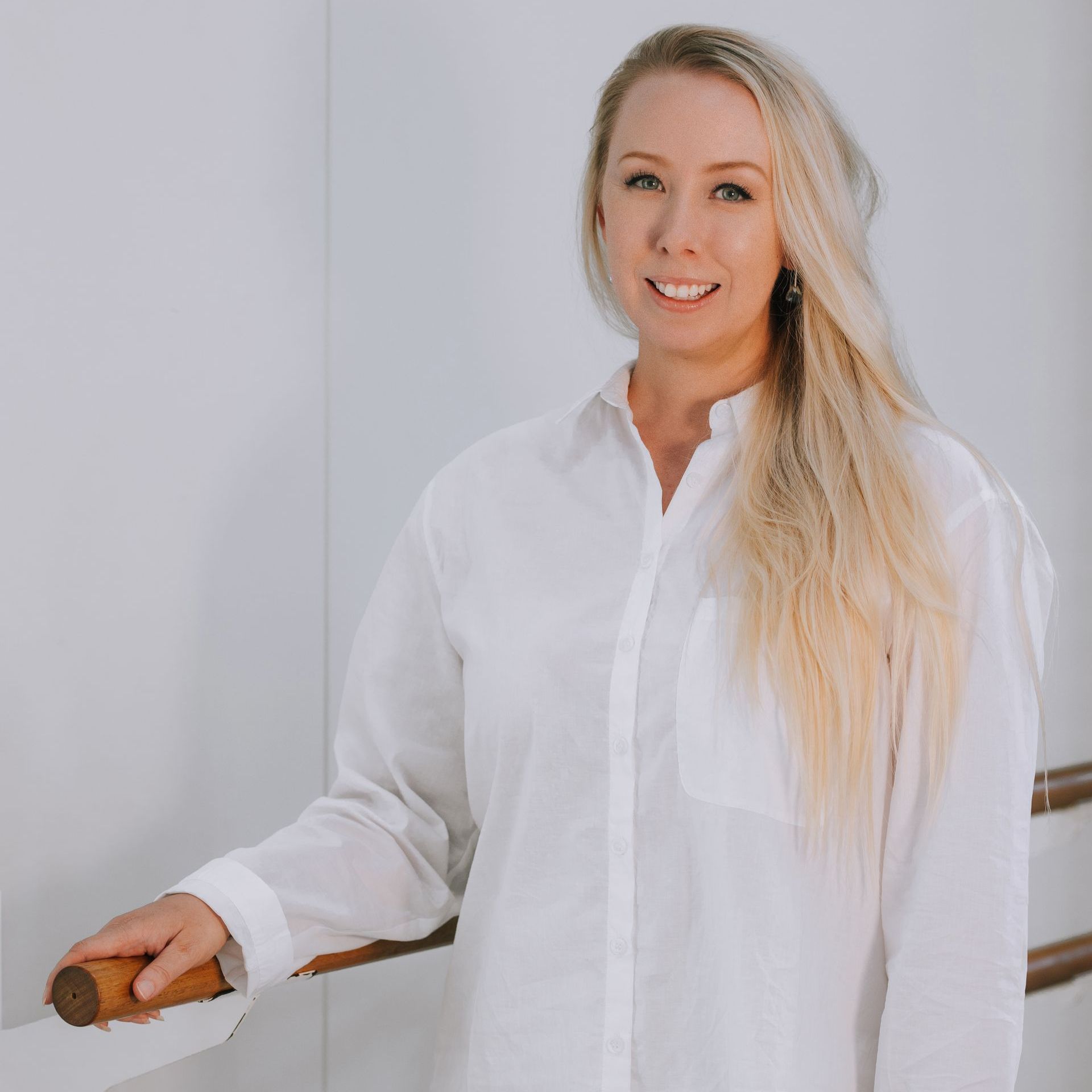 A woman in a white shirt is standing next to a wooden railing.