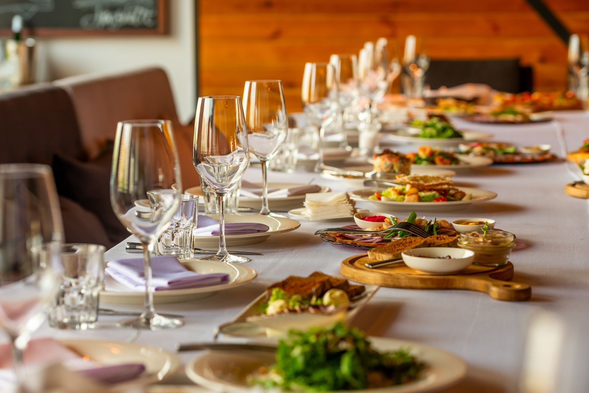 Long table set for a meal with plates of food, glasses, and a white tablecloth. Long table set for a meal with plates of food, glasses, and a white tablecloth.
