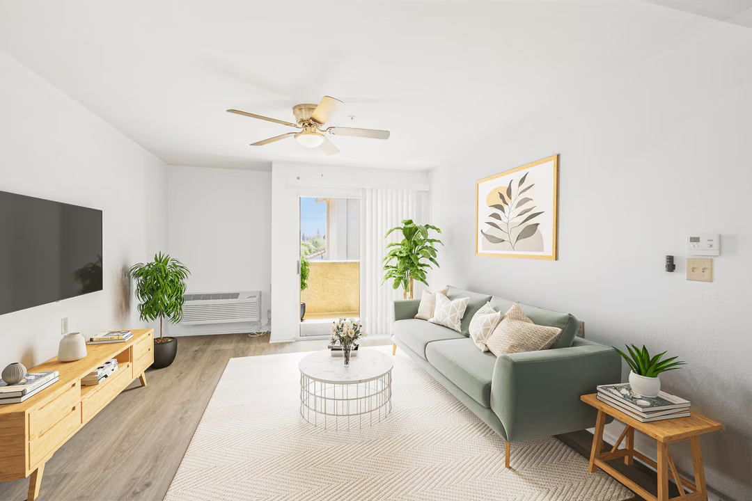 Bright modern living room with gray sofa, wall-mounted TV, plants, and large window doors.