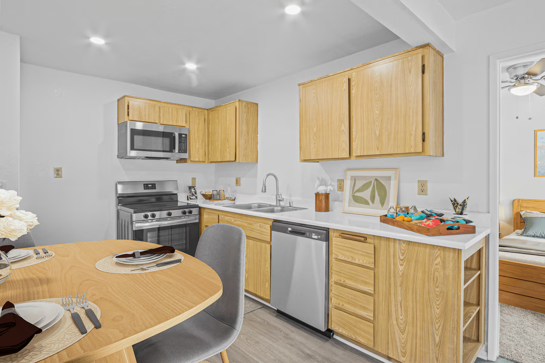 Bright kitchen with light wood cabinets, stainless appliances, and a round dining table in the foreground