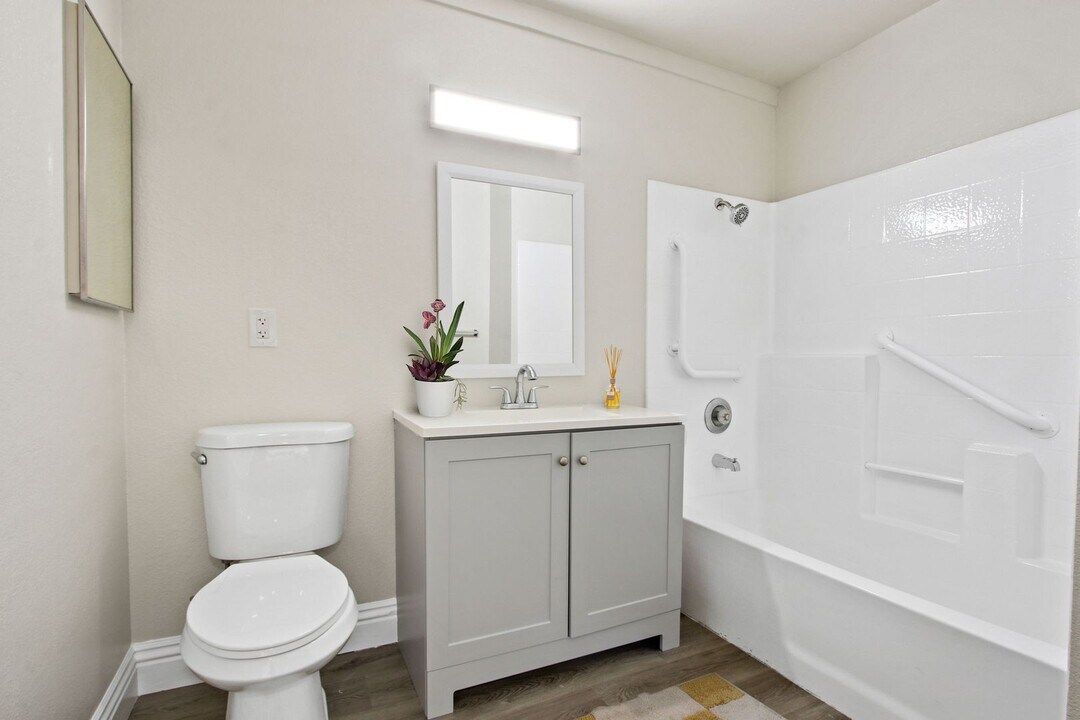 Bright white bathroom with toilet, vanity, mirror, and shower-tub combo