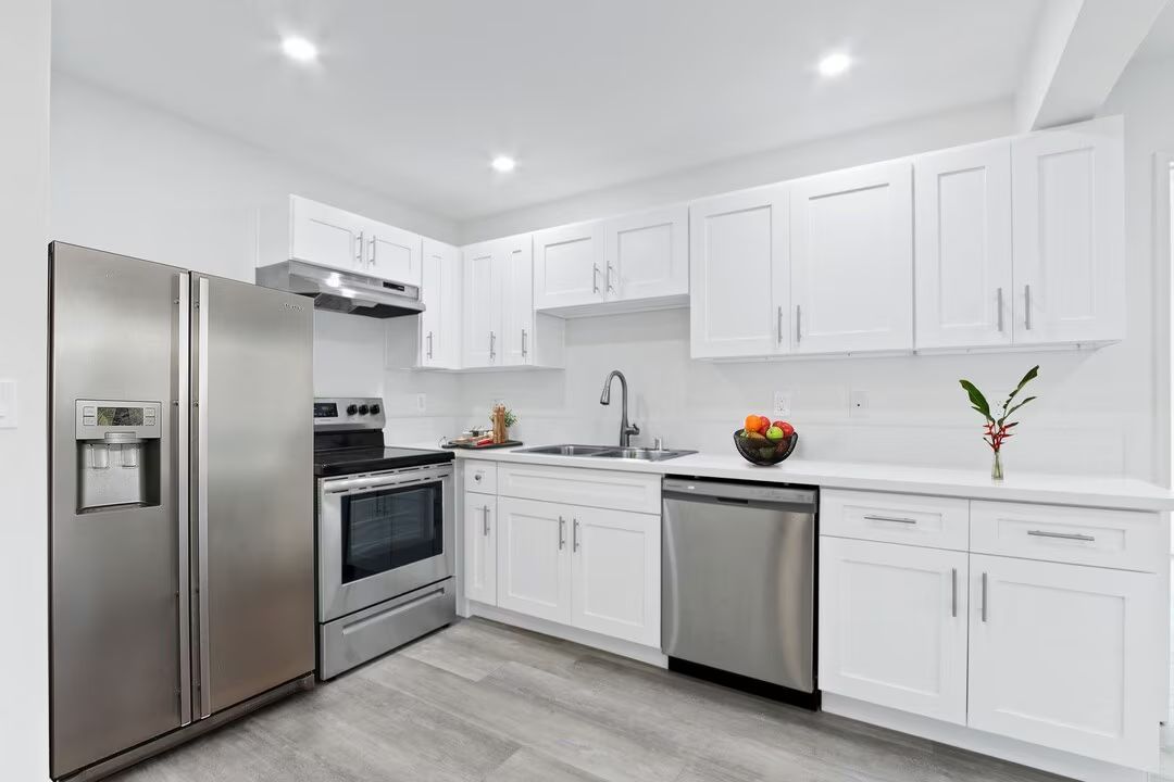 Modern white kitchen with stainless steel appliances, gray flooring, and a marble countertop