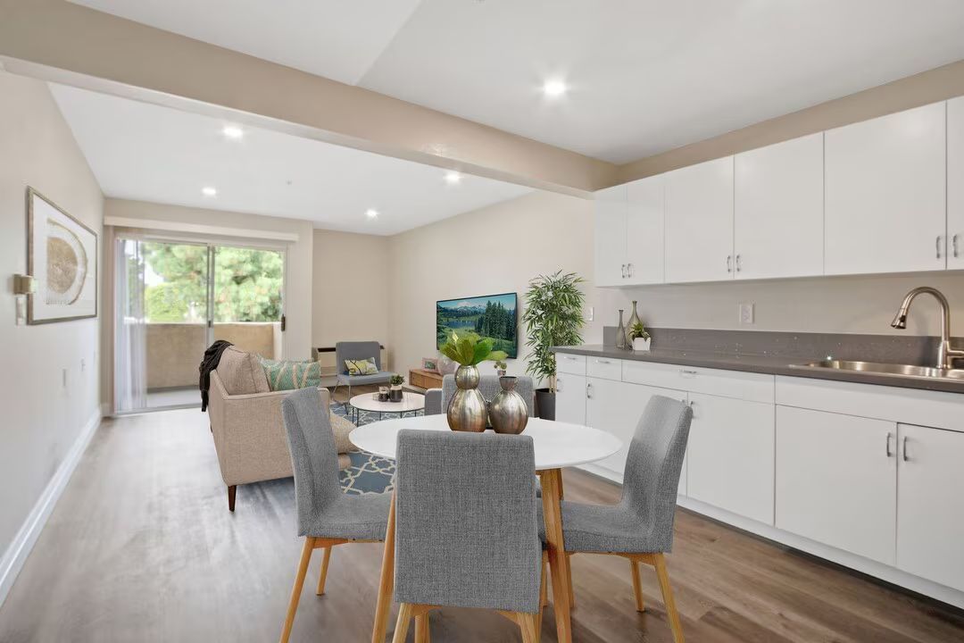Bright modern dining room and kitchen with white cabinets, wood floors, and a table near a large window