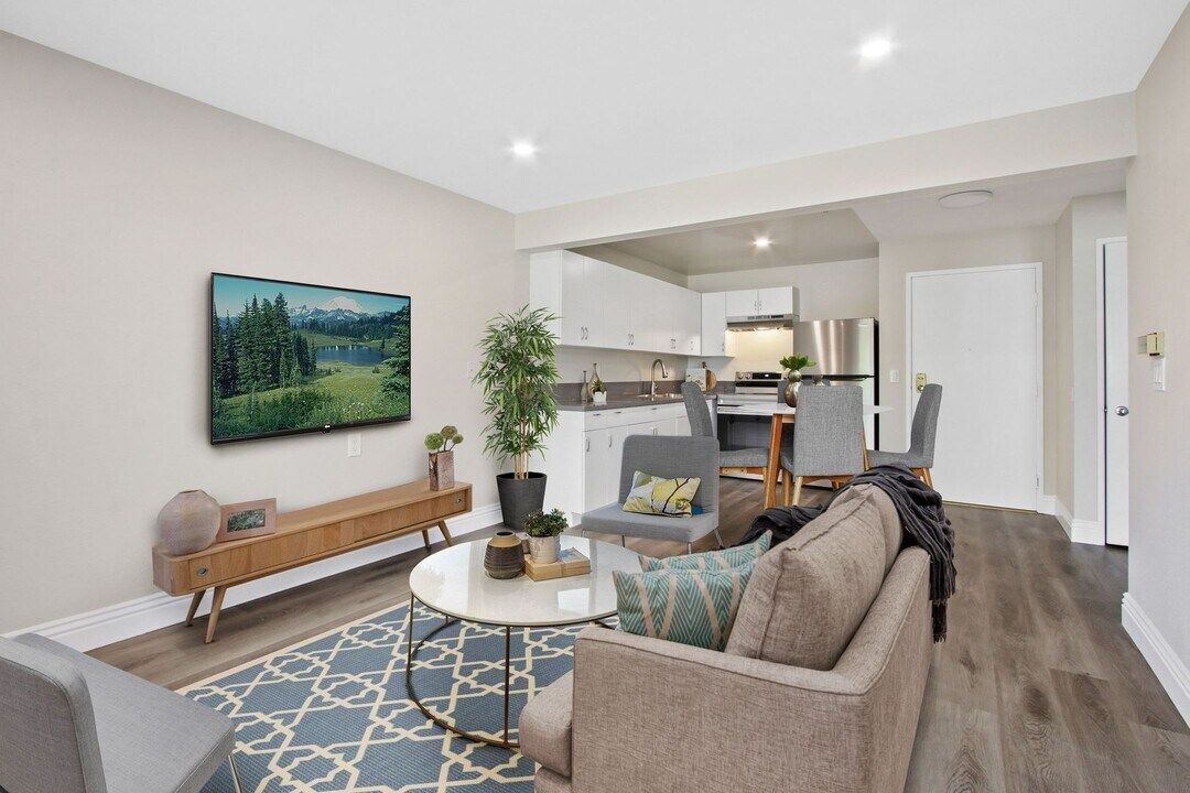 Modern living room with gray sofa, patterned rug, wall art, and open kitchen in the background