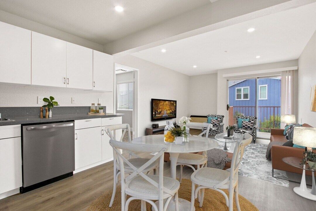 Bright open kitchen and living room with white cabinets, dining table, couch, and blue French doors