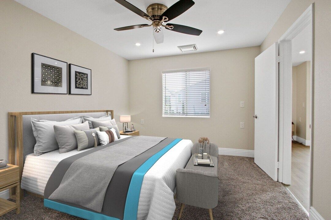 Bright bedroom with a bed, gray-and-blue bedding, ceiling fan, window, and mirrored closet doors.