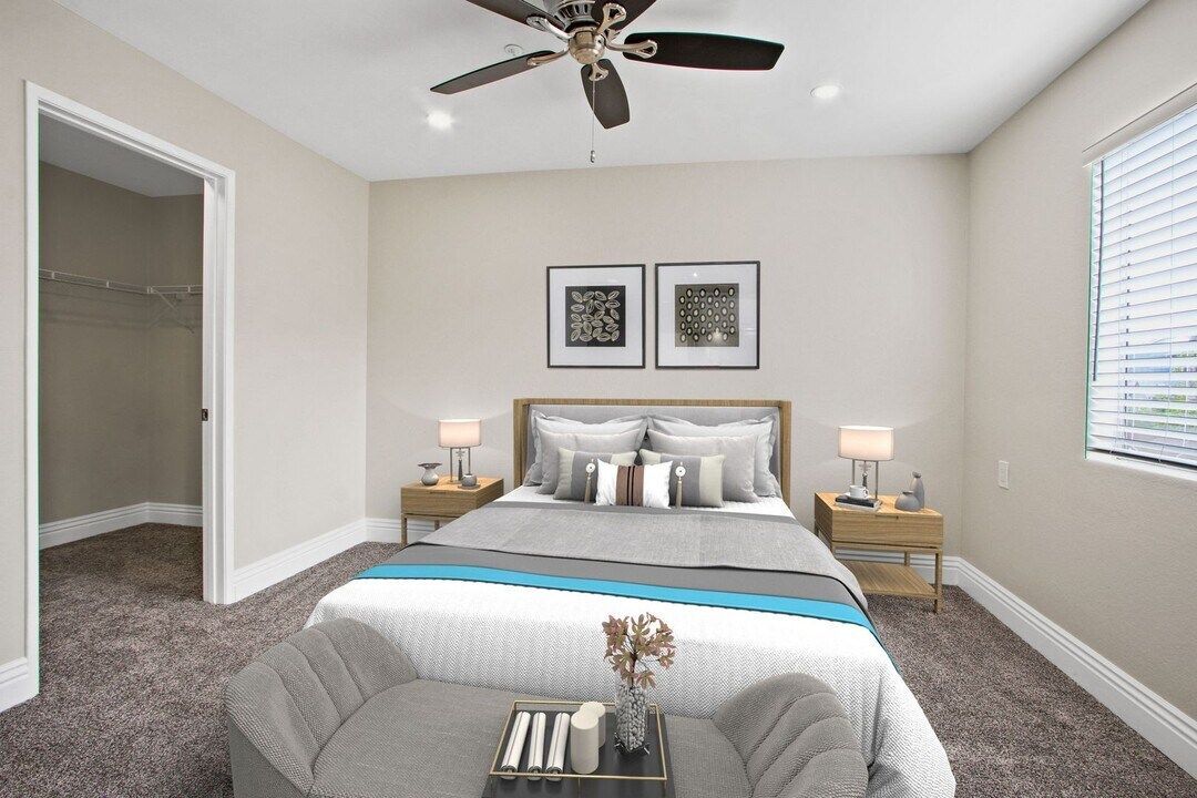 Bright bedroom with a bed, gray chair, ceiling fan, and open closet.