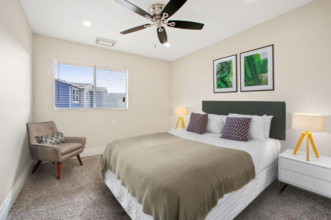 Bright bedroom with a bed, gray chair, nightstands, ceiling fan, and framed green artwork