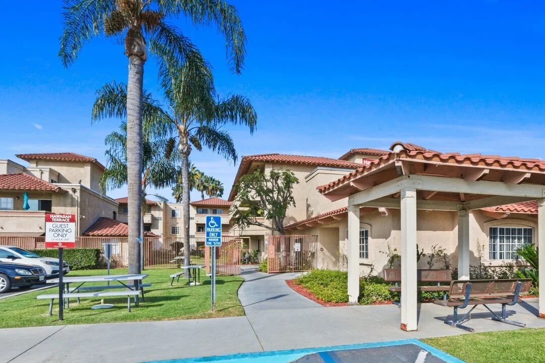 Apartment complex entrance with palm trees, covered walkway, and blue sky
