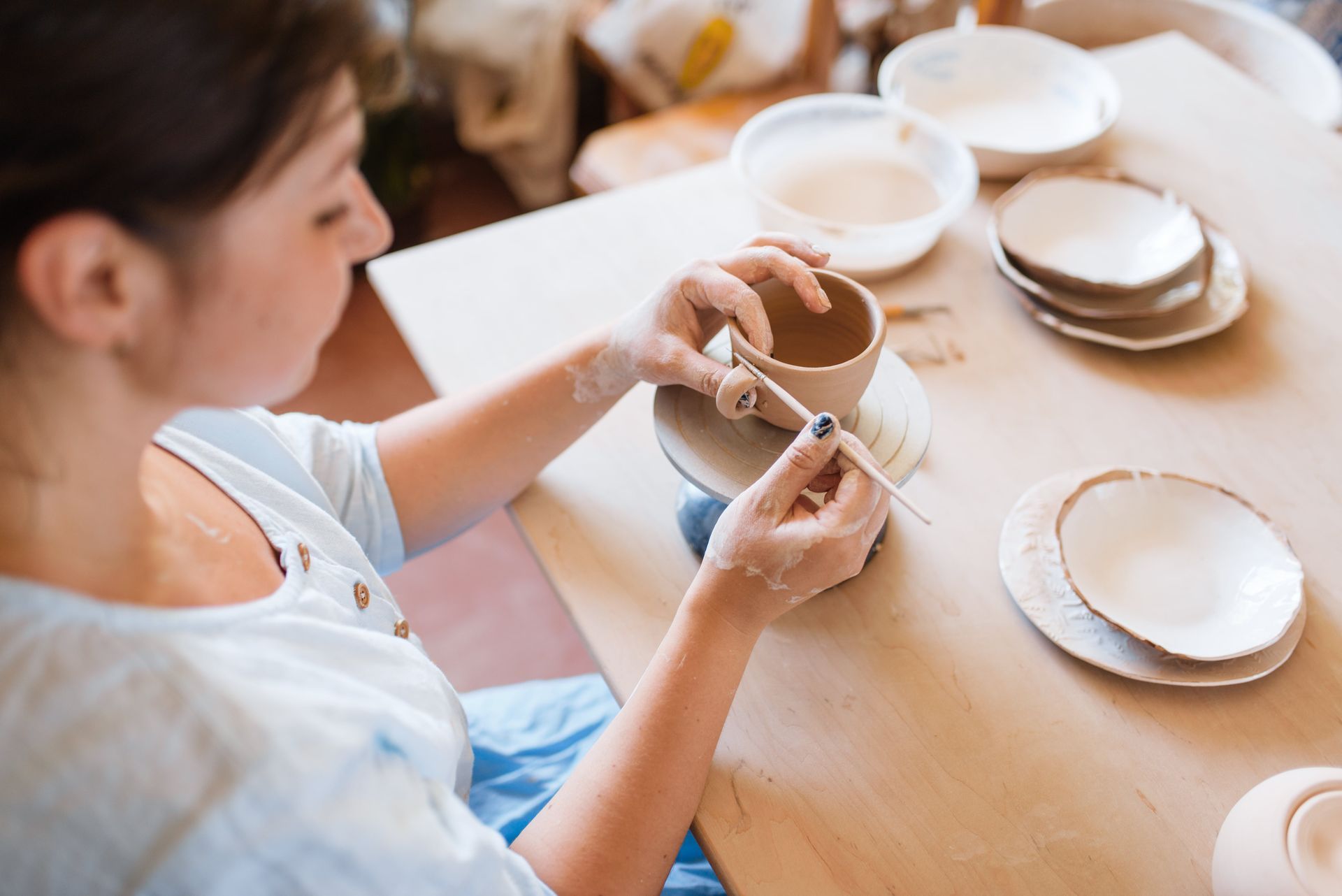 A woman is sitting at a table making pottery.